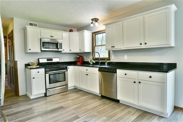 kitchen featuring dark countertops, a sink, light wood finished floors, stainless steel appliances, and visible vents