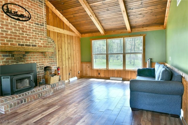 living room featuring wood walls, wood finished floors, baseboard heating, vaulted ceiling with beams, and wooden ceiling