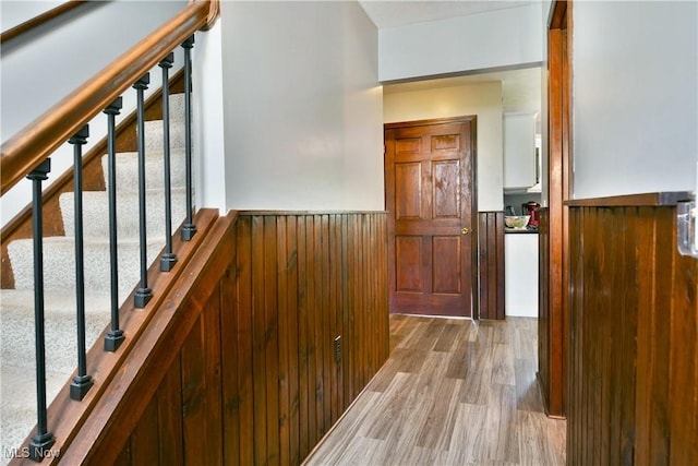 hall with stairs, wood walls, wainscoting, and wood finished floors