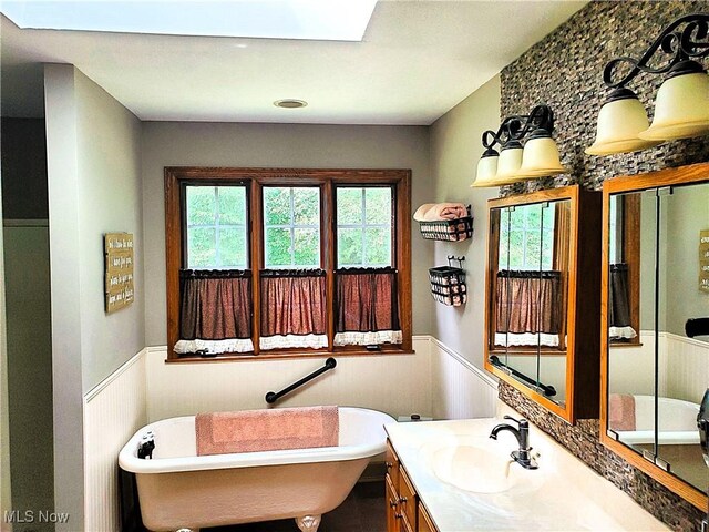 bathroom with a freestanding bath, vanity, plenty of natural light, and wainscoting