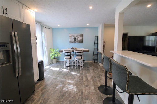 kitchen with stainless steel fridge with ice dispenser, baseboards, recessed lighting, white cabinetry, and dark wood-type flooring