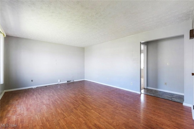 empty room featuring a textured ceiling, baseboards, wood finished floors, and visible vents