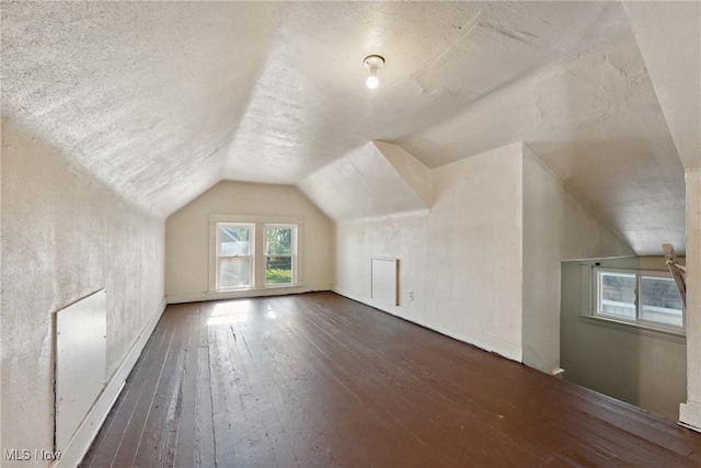 additional living space with a textured ceiling, hardwood / wood-style flooring, baseboards, and lofted ceiling