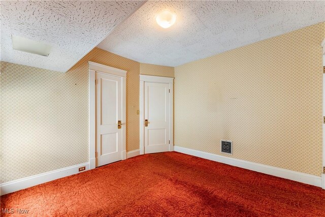 unfurnished bedroom with a textured ceiling, visible vents, baseboards, carpet, and wallpapered walls
