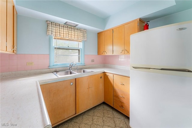 kitchen featuring tasteful backsplash, a sink, light countertops, freestanding refrigerator, and light floors