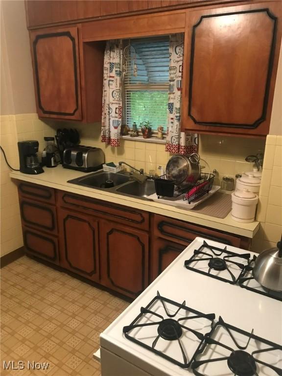 kitchen featuring light countertops, tile walls, wainscoting, and gas range gas stove