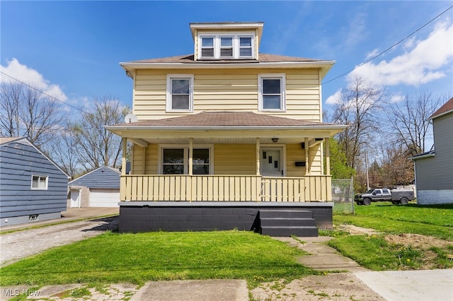 traditional style home with covered porch, a front yard, roof with shingles, an outbuilding, and a detached garage