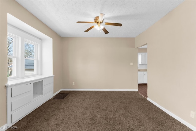empty room with a ceiling fan, baseboards, a textured ceiling, and dark colored carpet