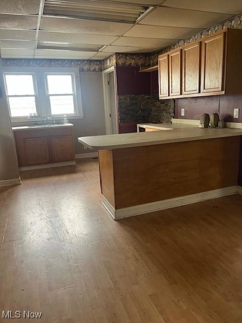 kitchen with brown cabinets, light countertops, baseboards, a peninsula, and light wood-style floors
