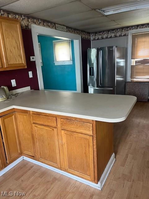 kitchen with light countertops, stainless steel fridge with ice dispenser, a peninsula, and light wood-style flooring