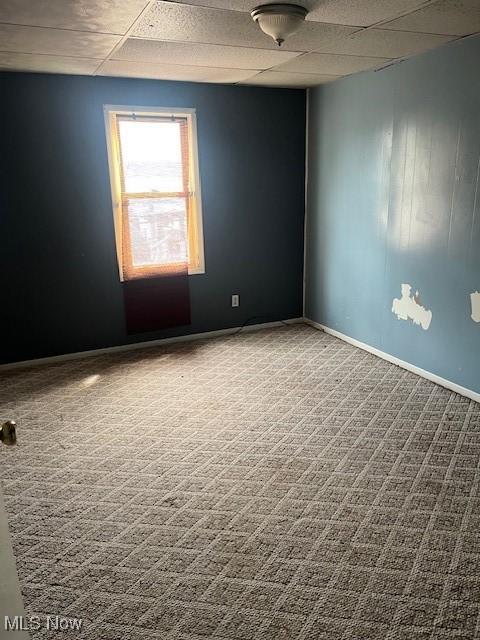 carpeted spare room featuring baseboards and a paneled ceiling