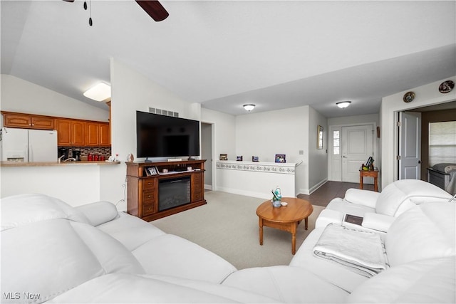 carpeted living area with visible vents, a glass covered fireplace, lofted ceiling, baseboards, and a ceiling fan