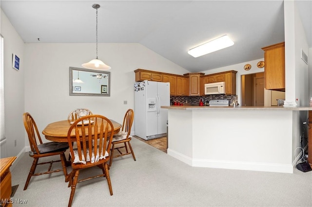 kitchen featuring brown cabinetry, vaulted ceiling, white appliances, and light carpet