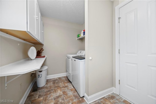 laundry area featuring stone finish floor, a textured ceiling, cabinet space, baseboards, and washer and dryer