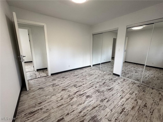 unfurnished bedroom with baseboards, multiple closets, and wood finished floors