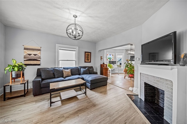living area featuring a textured ceiling, an inviting chandelier, wood finished floors, and a fireplace