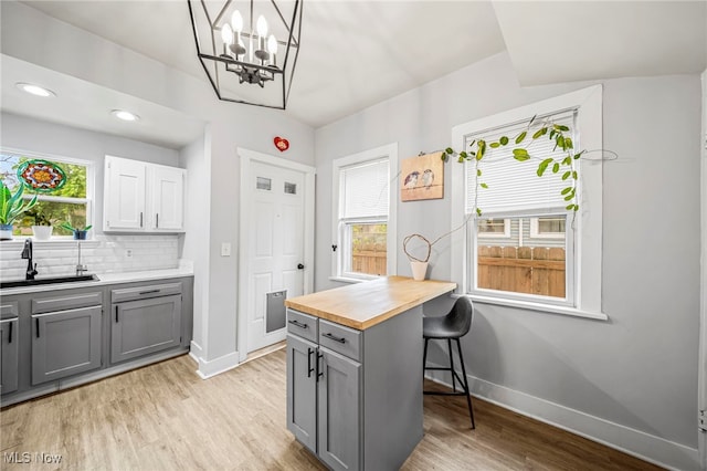 kitchen featuring a sink, light wood-style floors, wooden counters, gray cabinets, and baseboards