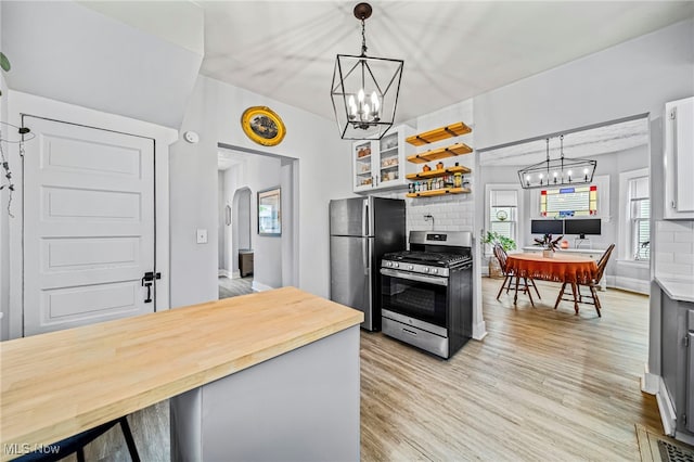 kitchen featuring decorative backsplash, light wood finished floors, a notable chandelier, decorative light fixtures, and stainless steel appliances