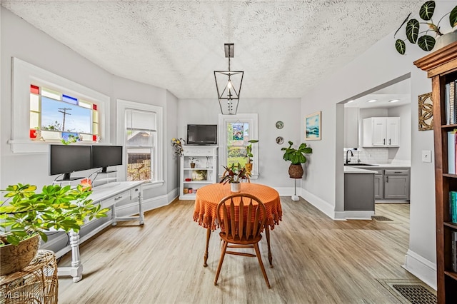 dining area with a textured ceiling, baseboards, and light wood finished floors