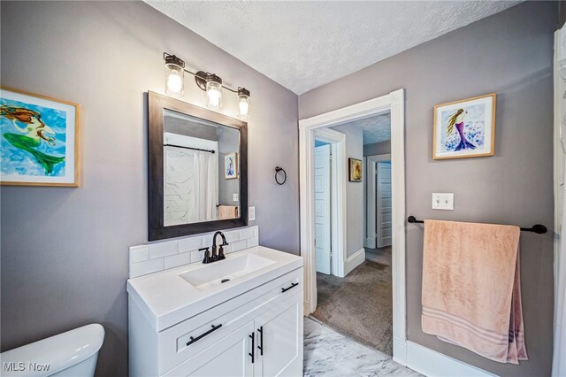 full bath with a textured ceiling, vanity, baseboards, toilet, and marble finish floor