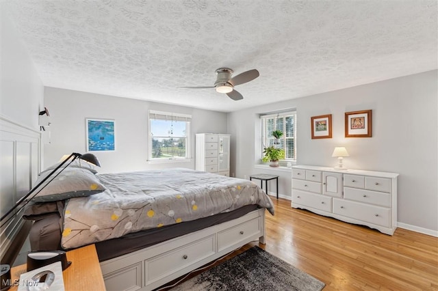bedroom with baseboards, a textured ceiling, ceiling fan, and light wood-style flooring