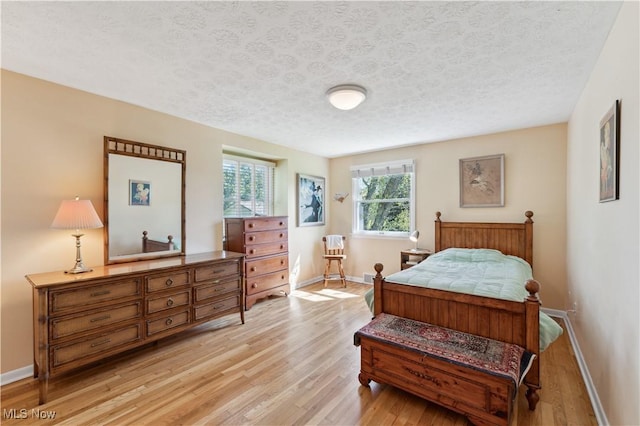 bedroom featuring light wood-type flooring, a textured ceiling, and baseboards