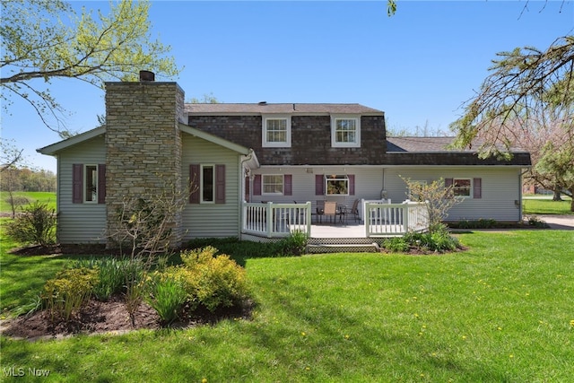 rear view of property with a yard, a deck, a chimney, and roof with shingles