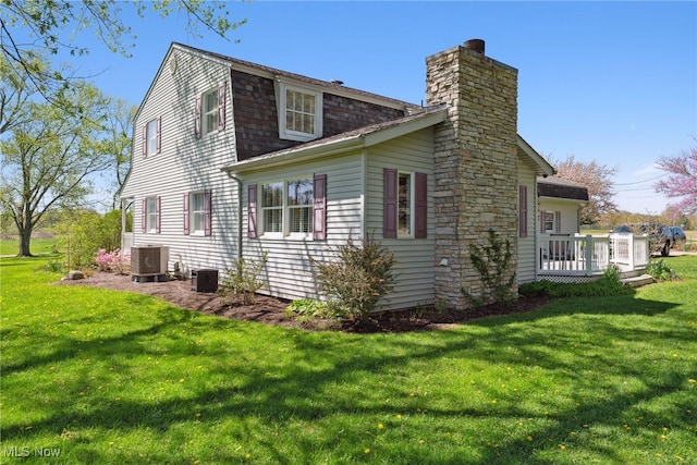 view of side of property with a yard, a deck, cooling unit, and a chimney