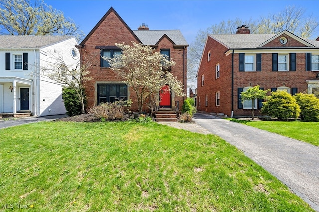 view of front of home featuring brick siding, a chimney, and a front lawn