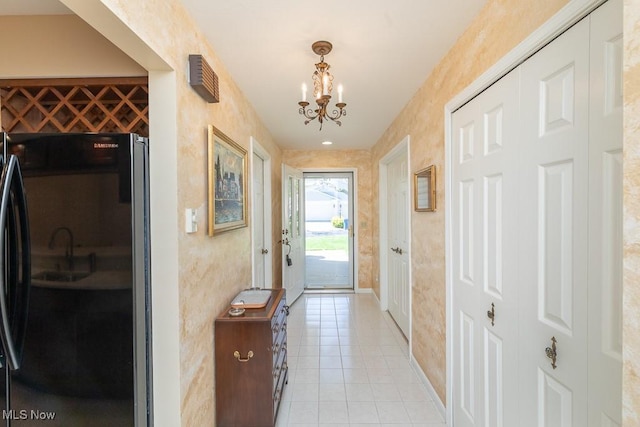 doorway with an inviting chandelier, baseboards, and light tile patterned flooring