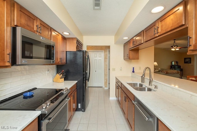 kitchen with brown cabinets, a sink, stainless steel appliances, a ceiling fan, and backsplash