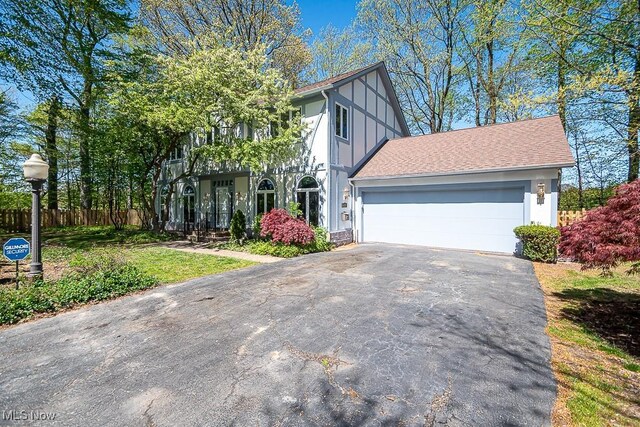 view of front of property with board and batten siding, a garage, fence, aphalt driveway, and a shingled roof