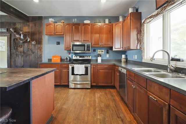 kitchen with a sink, appliances with stainless steel finishes, dark countertops, and dark wood-type flooring