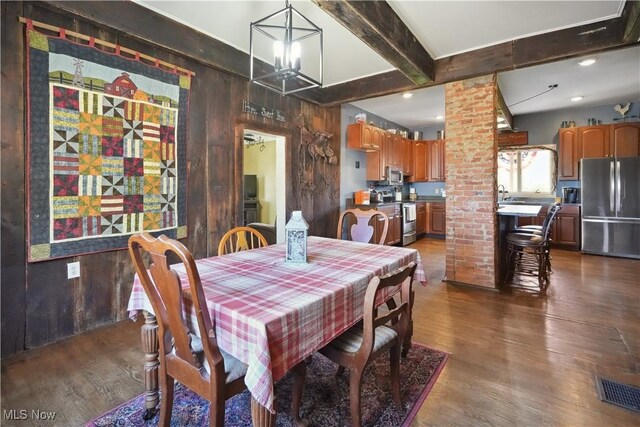 dining room featuring an inviting chandelier, dark wood-style flooring, wood walls, and beam ceiling
