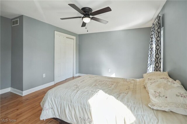 bedroom featuring a ceiling fan, visible vents, wood finished floors, baseboards, and a closet