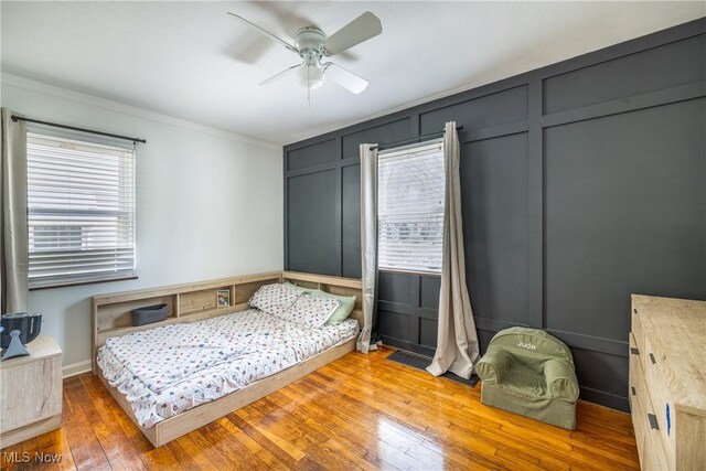bedroom featuring crown molding, a ceiling fan, hardwood / wood-style floors, and a decorative wall