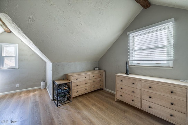 bonus room featuring a textured ceiling, baseboards, lofted ceiling with beams, and light wood-style flooring
