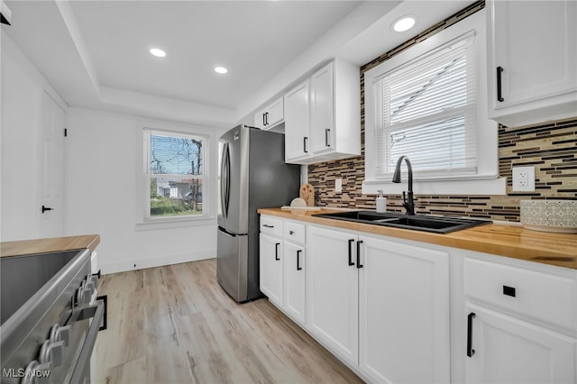 kitchen featuring a sink, light wood-style floors, stainless steel appliances, tasteful backsplash, and butcher block counters