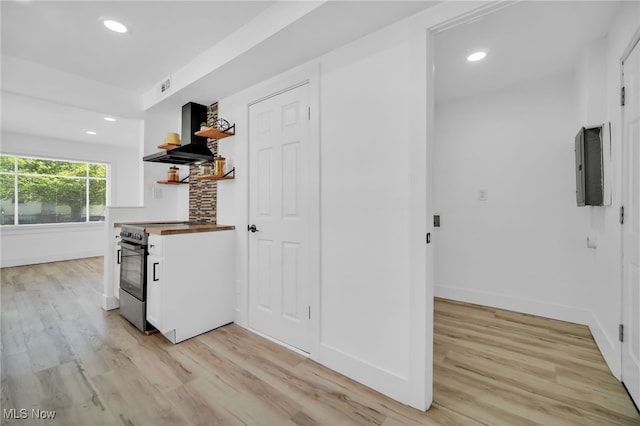 kitchen with open shelves, stainless steel range with electric cooktop, white cabinets, light wood finished floors, and wall chimney exhaust hood