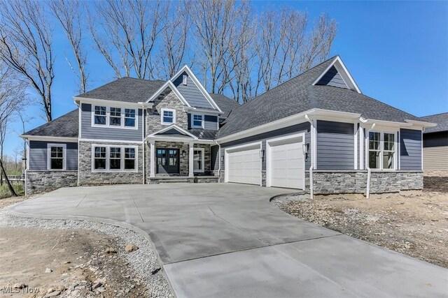 craftsman-style house featuring roof with shingles, an attached garage, driveway, and stone siding
