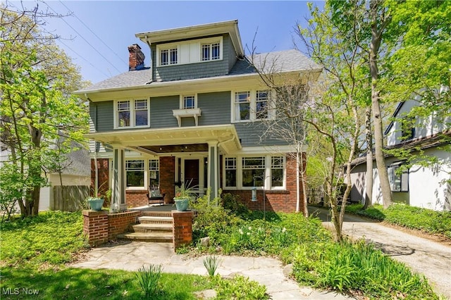 traditional style home with fence, covered porch, a chimney, brick siding, and driveway