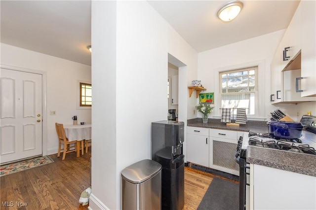 kitchen featuring dark countertops, gas stove, baseboards, white cabinets, and light wood finished floors