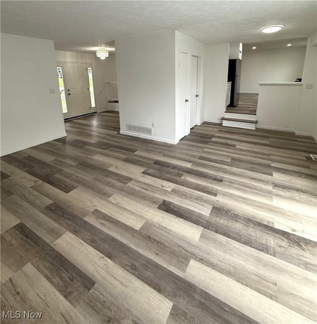 spare room with visible vents, stairs, wood finished floors, baseboards, and a textured ceiling