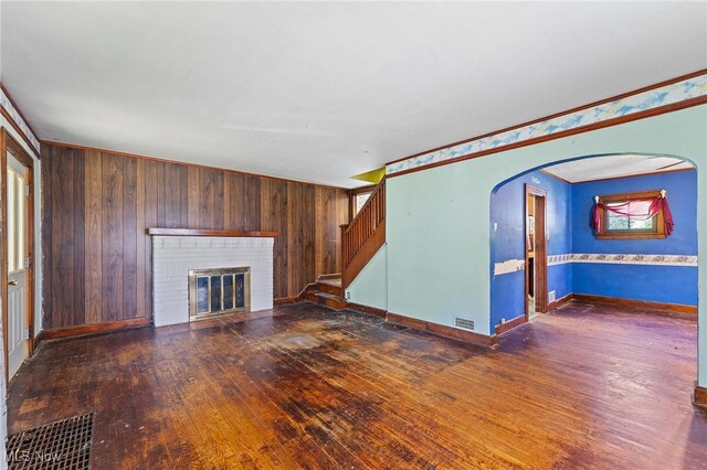 unfurnished living room featuring wood-type flooring, stairs, a brick fireplace, and baseboards
