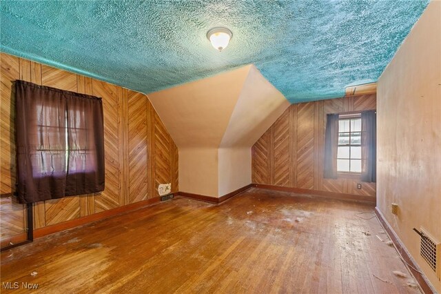 additional living space featuring visible vents, wood walls, baseboards, wood-type flooring, and lofted ceiling