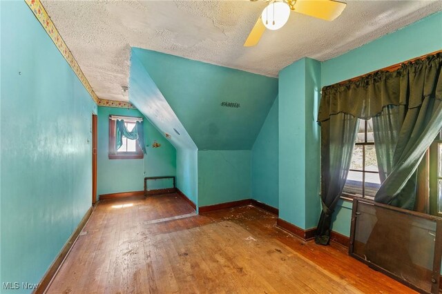 additional living space featuring a textured ceiling, hardwood / wood-style floors, a ceiling fan, baseboards, and lofted ceiling