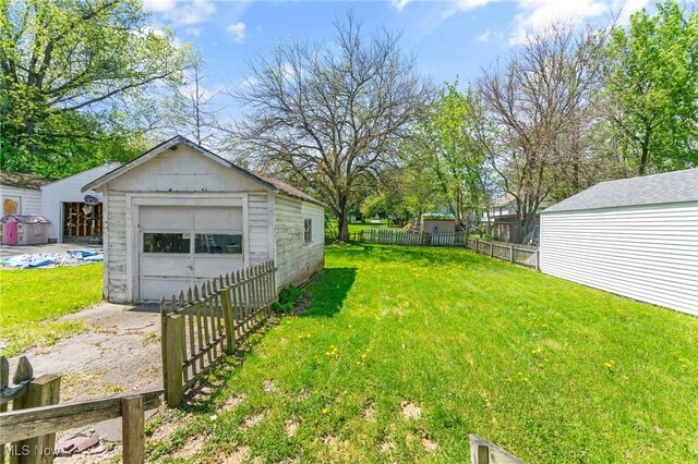view of yard featuring a garage, an outbuilding, fence, and driveway