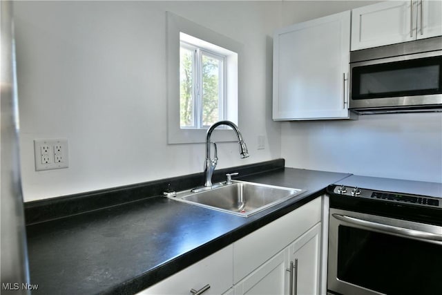 kitchen with white cabinets, dark countertops, appliances with stainless steel finishes, and a sink