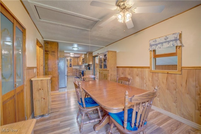 dining space featuring wooden walls, light wood-style flooring, and a wainscoted wall