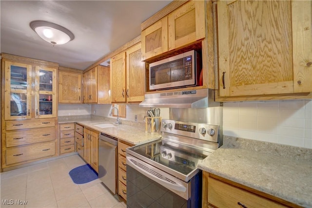 kitchen with a sink, stainless steel appliances, backsplash, light tile patterned floors, and under cabinet range hood
